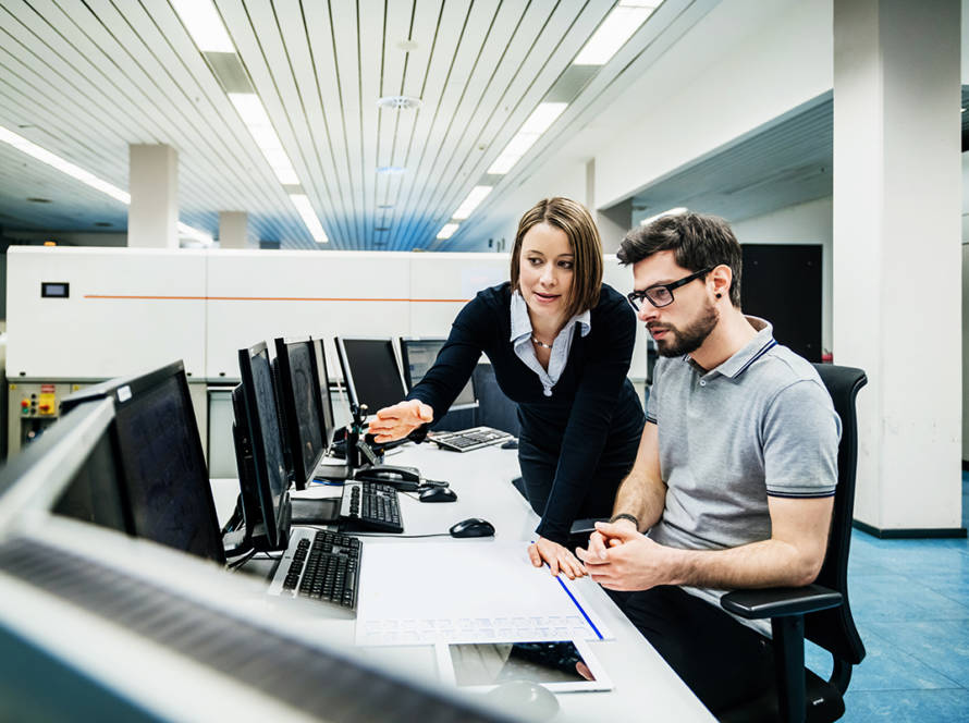 A female and a male in an office environment looking at a computer monitor
