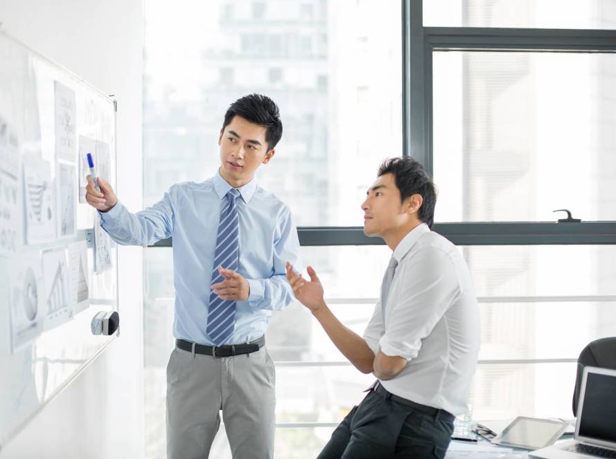 Two male standing in front of a white board having discussions